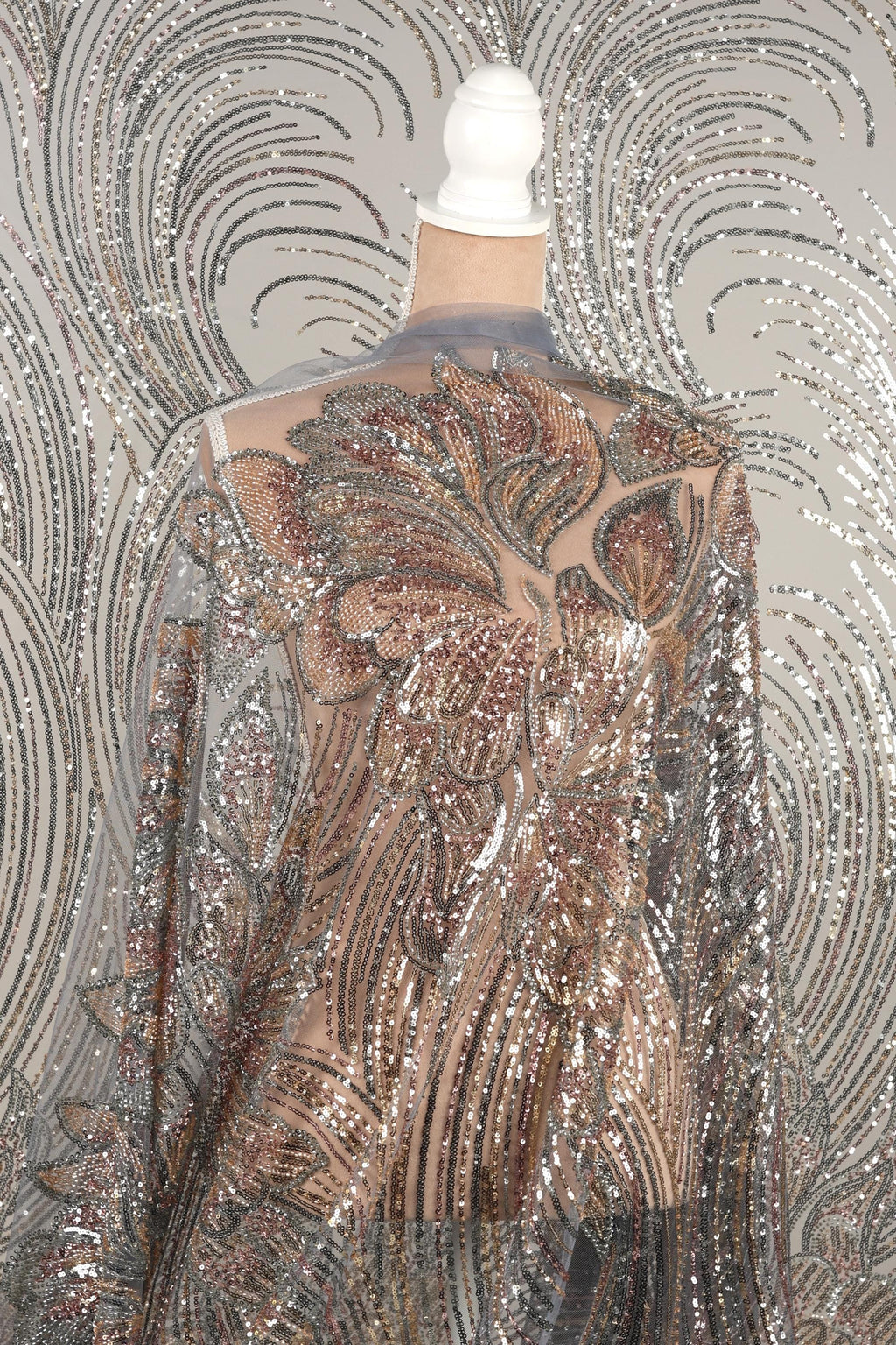a mannequin wearing a shimmering, sequined dress with a floral pattern. The dress has a sheer back and long sleeves, giving it a delicate and elegant appearance.