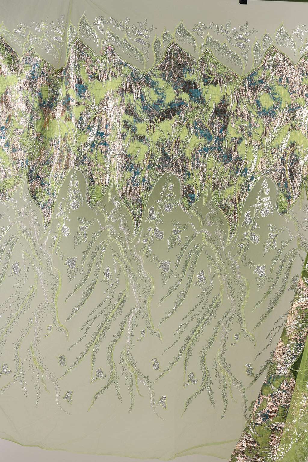 a close-up view of a fabric with a floral pattern, including green and silver elements. The fabric appears to be a sheer material, with a delicate and intricate design.