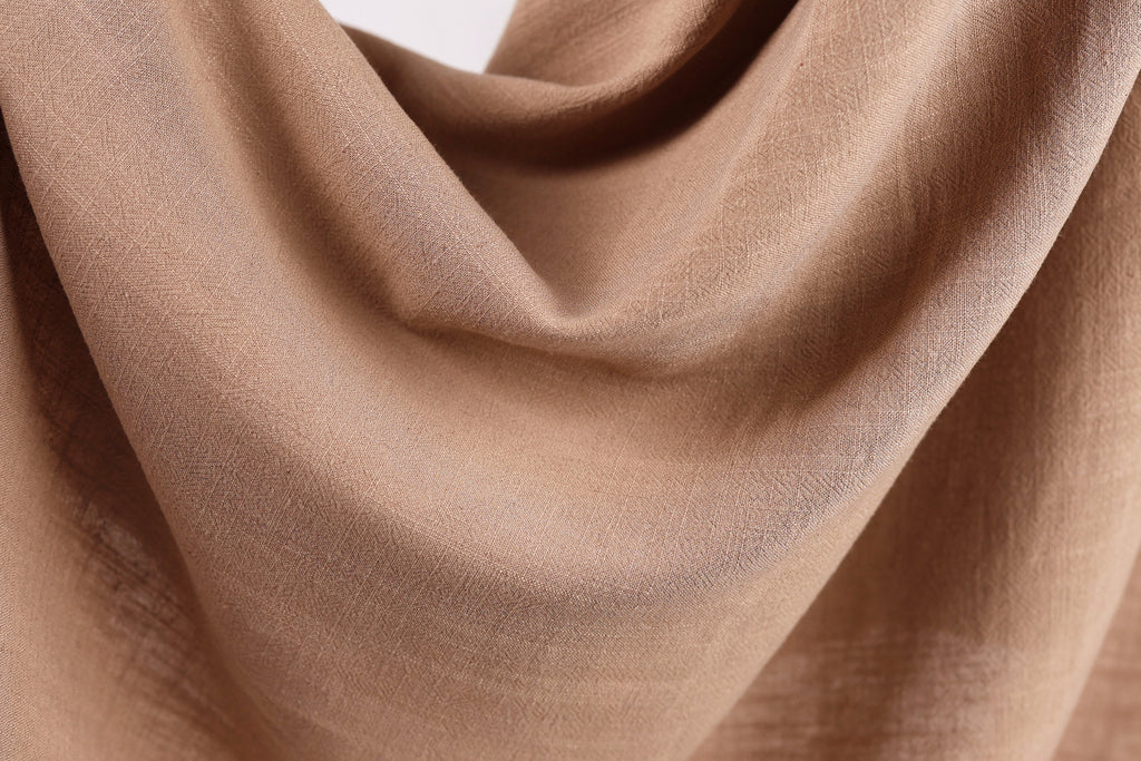 A close-up view of a brown fabric, possibly a piece of clothing or a textile, with a soft, crumpled texture.