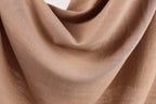 A close-up view of a brown fabric, possibly a piece of clothing or a textile, with a soft, crumpled texture.