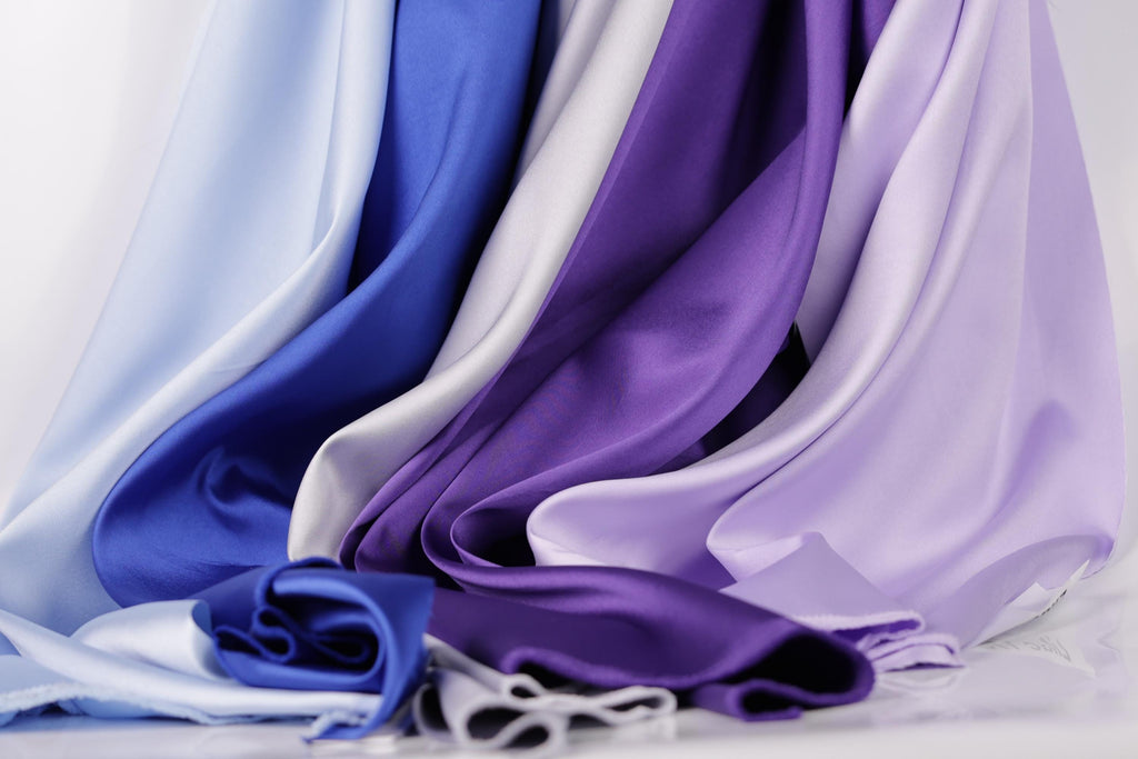 a variety of colorful satin fabrics, including blue, purple, and white, arranged in a visually appealing manner.