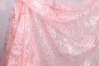 a close-up view of a delicate, pink lace fabric with a floral pattern. The fabric appears to be made of sheer material, giving it a soft and delicate appearance. The lace is intricately designed with a repeating pattern of leaves and flowers, creating a visually appealing and elegant design.