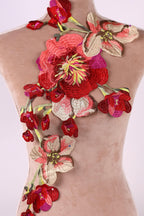 a mannequin with a beige dress adorned with a large, intricately embroidered floral design. The design consists of a variety of red and pink flowers, including a prominent red rose, arranged in a cascading manner. The embroidery appears to be done with a high level of detail and craftsmanship, creating a visually striking and elegant appearance.