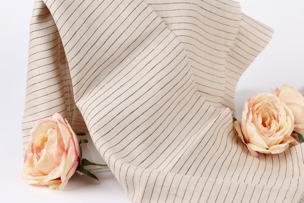 A beige fabric with black stripes is draped over a white background, with two delicate pink roses resting on either side of the fabric.
