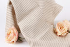 A beige fabric with black stripes is draped over a white background, with two delicate pink roses resting on either side of the fabric.