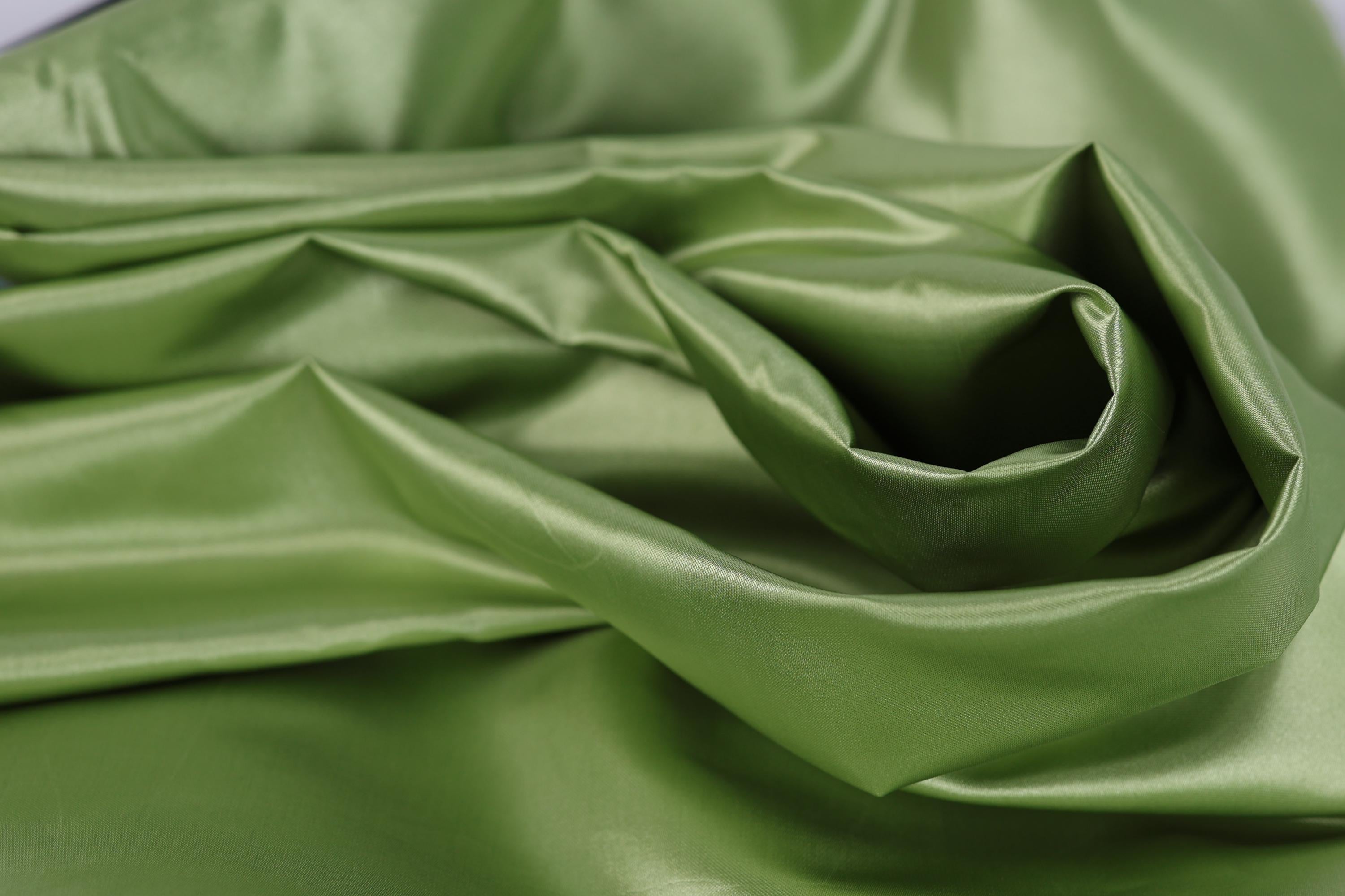 A close-up view of a crumpled, shiny green fabric, possibly silk or satin, with a smooth, shiny texture.