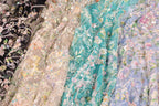 a variety of colorful, intricately embroidered fabric pieces, including a teal fabric with a floral pattern and a black fabric with a floral pattern. The fabric pieces are arranged in a row, showcasing the different designs and colors.