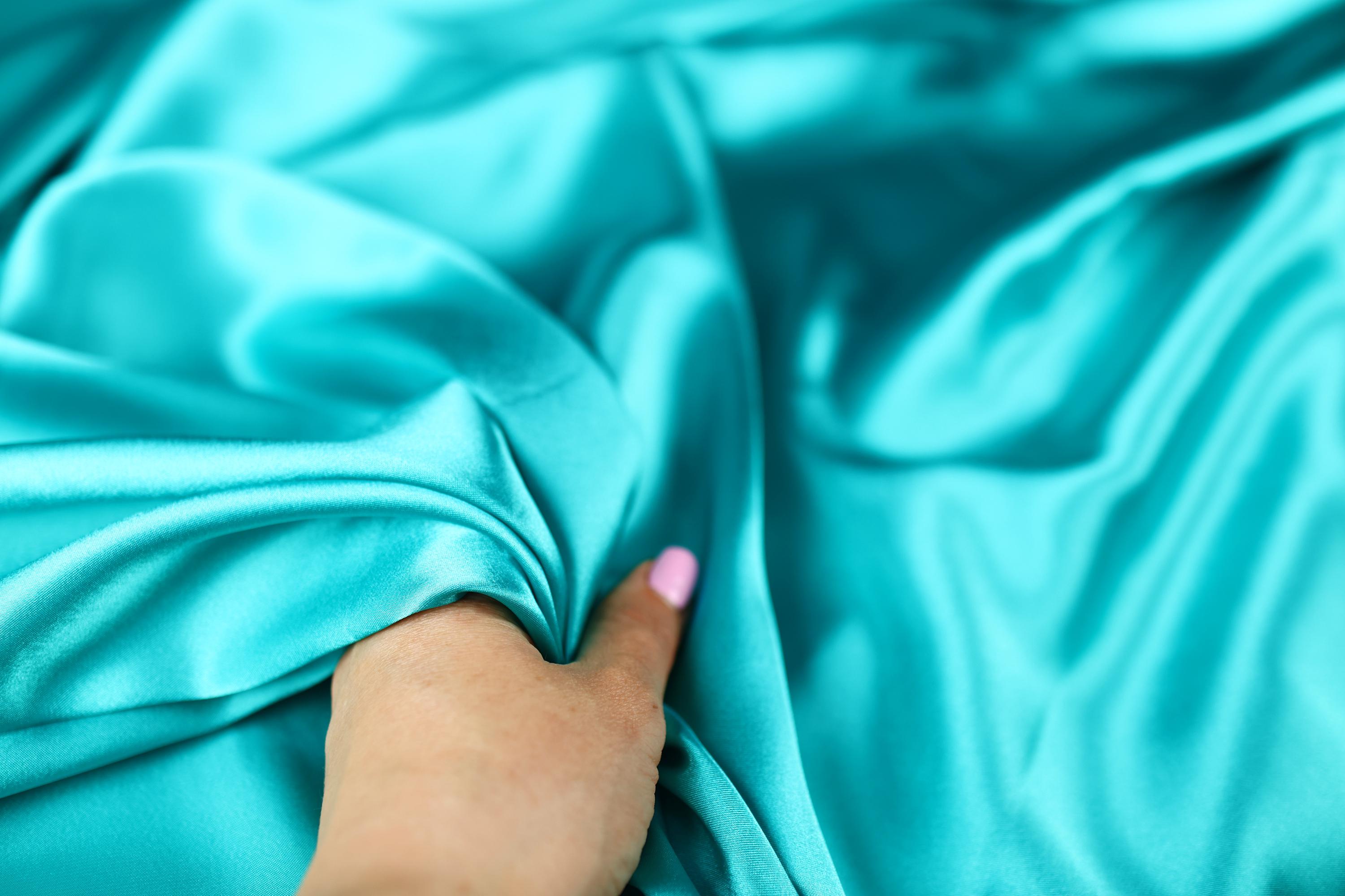 a woman&#39;s hand on a blue satin material
