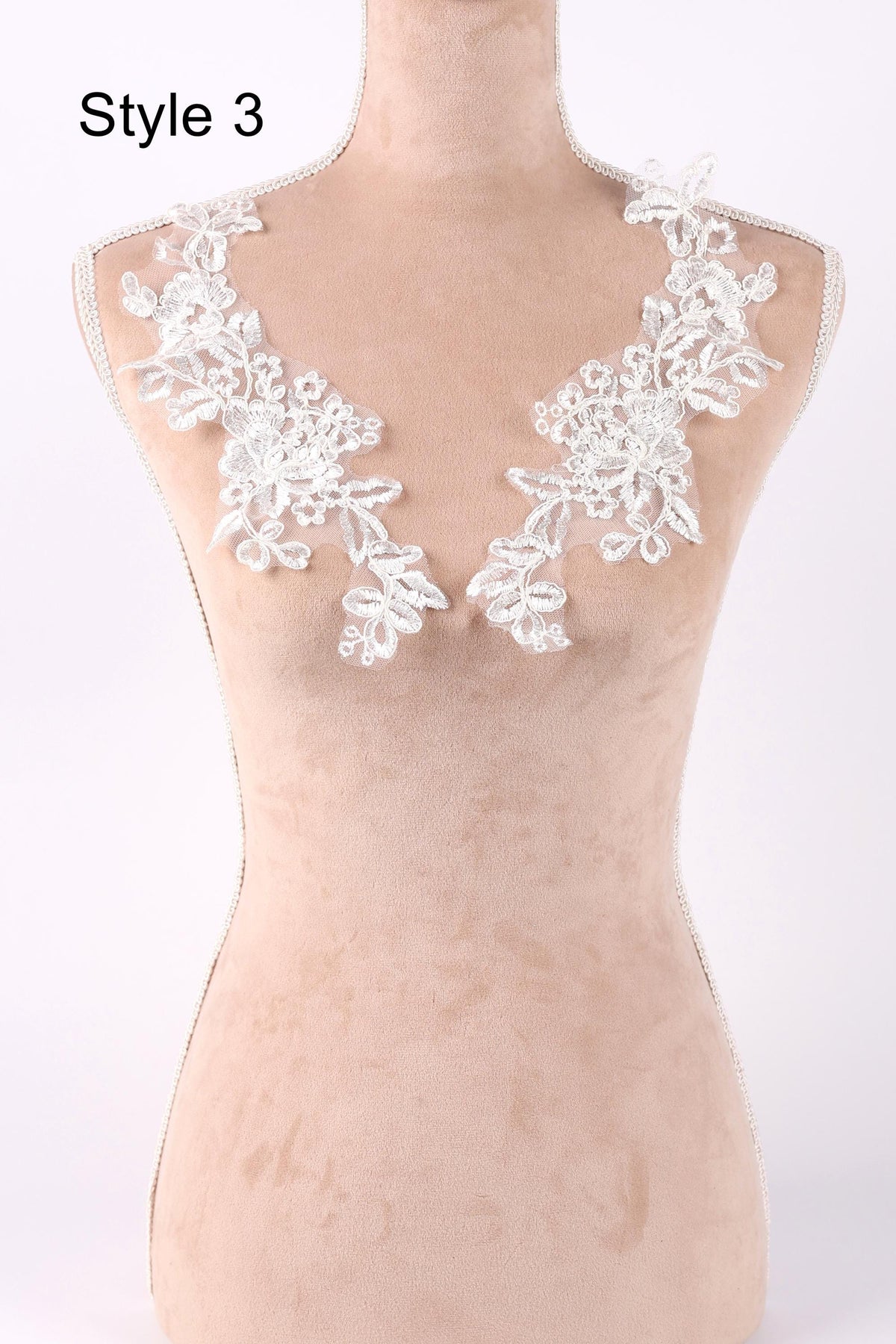 A mannequin wearing a beige dress with white lace flowers on the neckline.