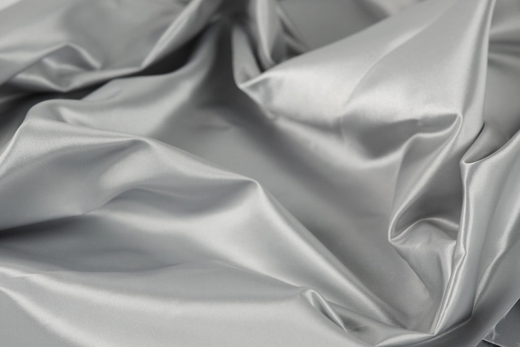 The image is a close-up of a crumpled, shiny, and smooth grey fabric, possibly silk or satin.