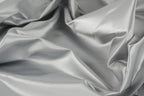 The image is a close-up of a crumpled, shiny, and smooth grey fabric, possibly silk or satin.