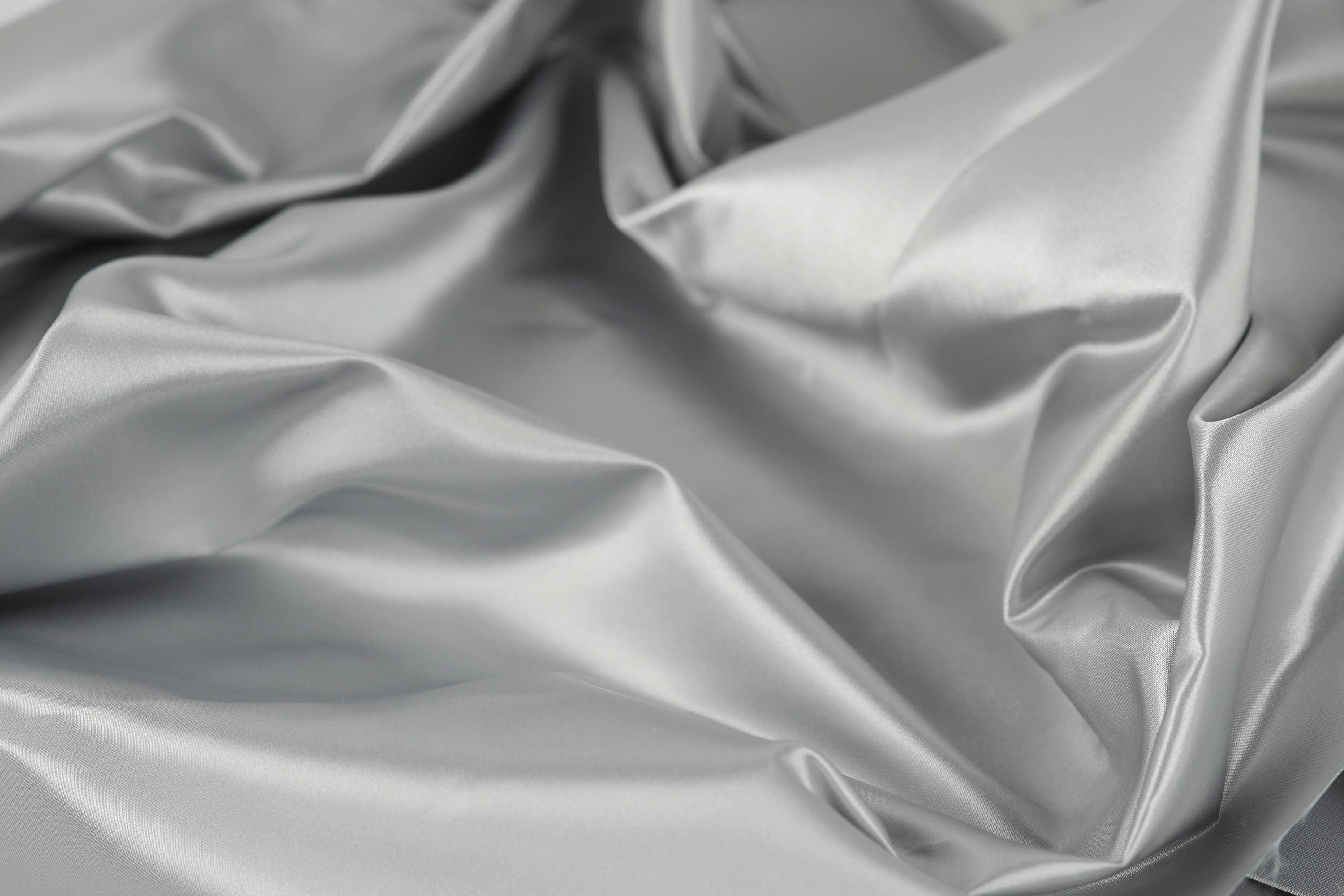 The image is a close-up of a crumpled, shiny, and smooth grey fabric, possibly silk or satin.