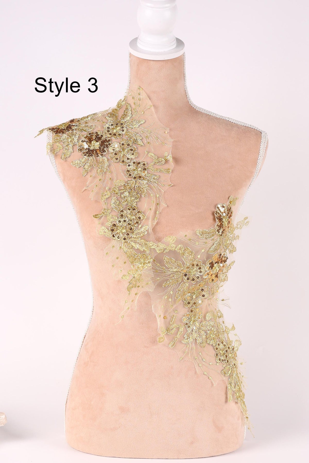 A mannequin with a decorative gold and beige floral lace overlay on its shoulder.