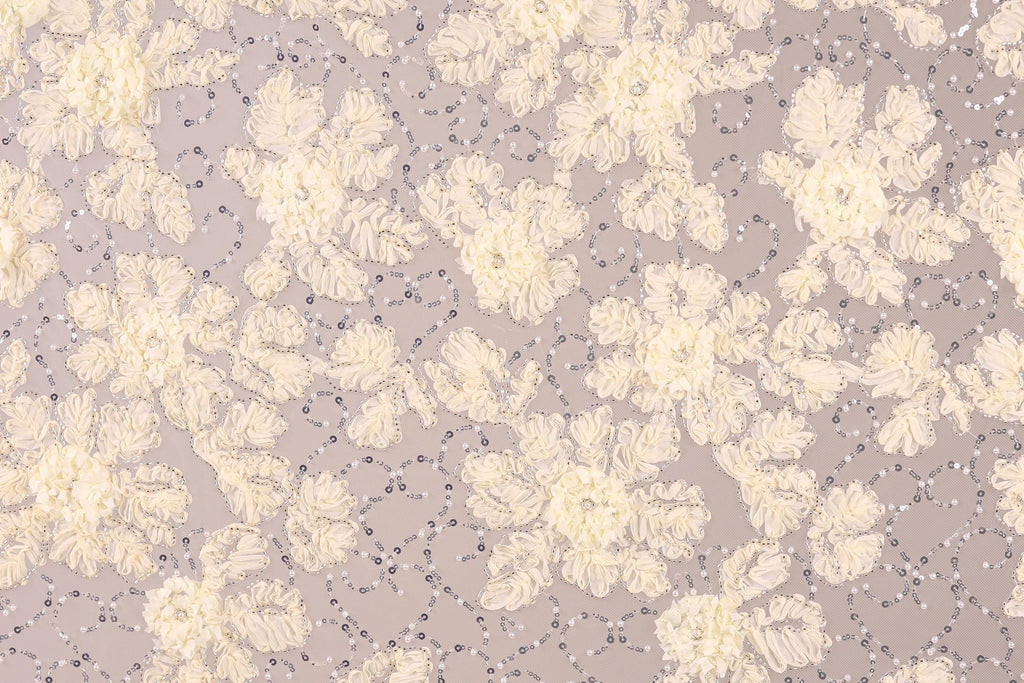 a close-up view of a fabric with a floral pattern, including white and beige flowers and small silver sequins or beads scattered throughout the fabric.
