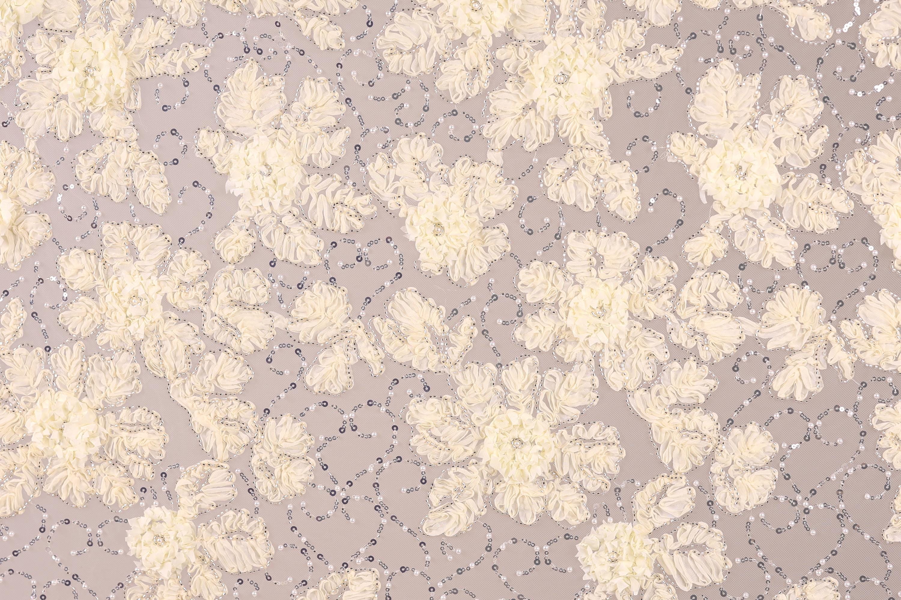 a close-up view of a fabric with a floral pattern, including white and beige flowers and small silver sequins or beads scattered throughout the fabric.