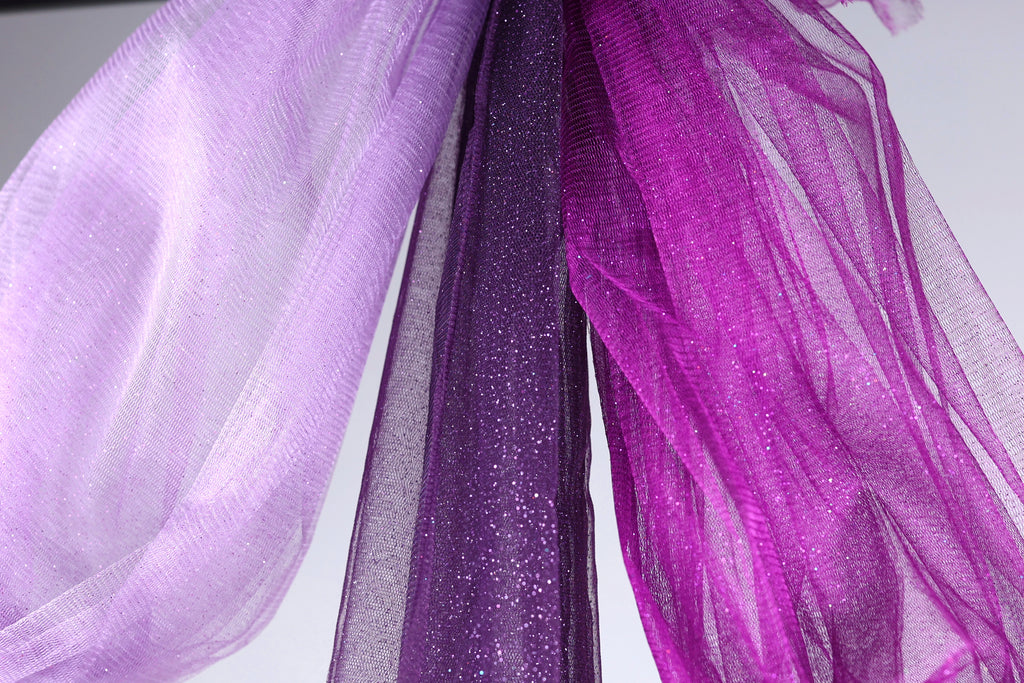 a close-up view of a fabric with a purple and white color scheme, featuring a shiny, glittery texture.