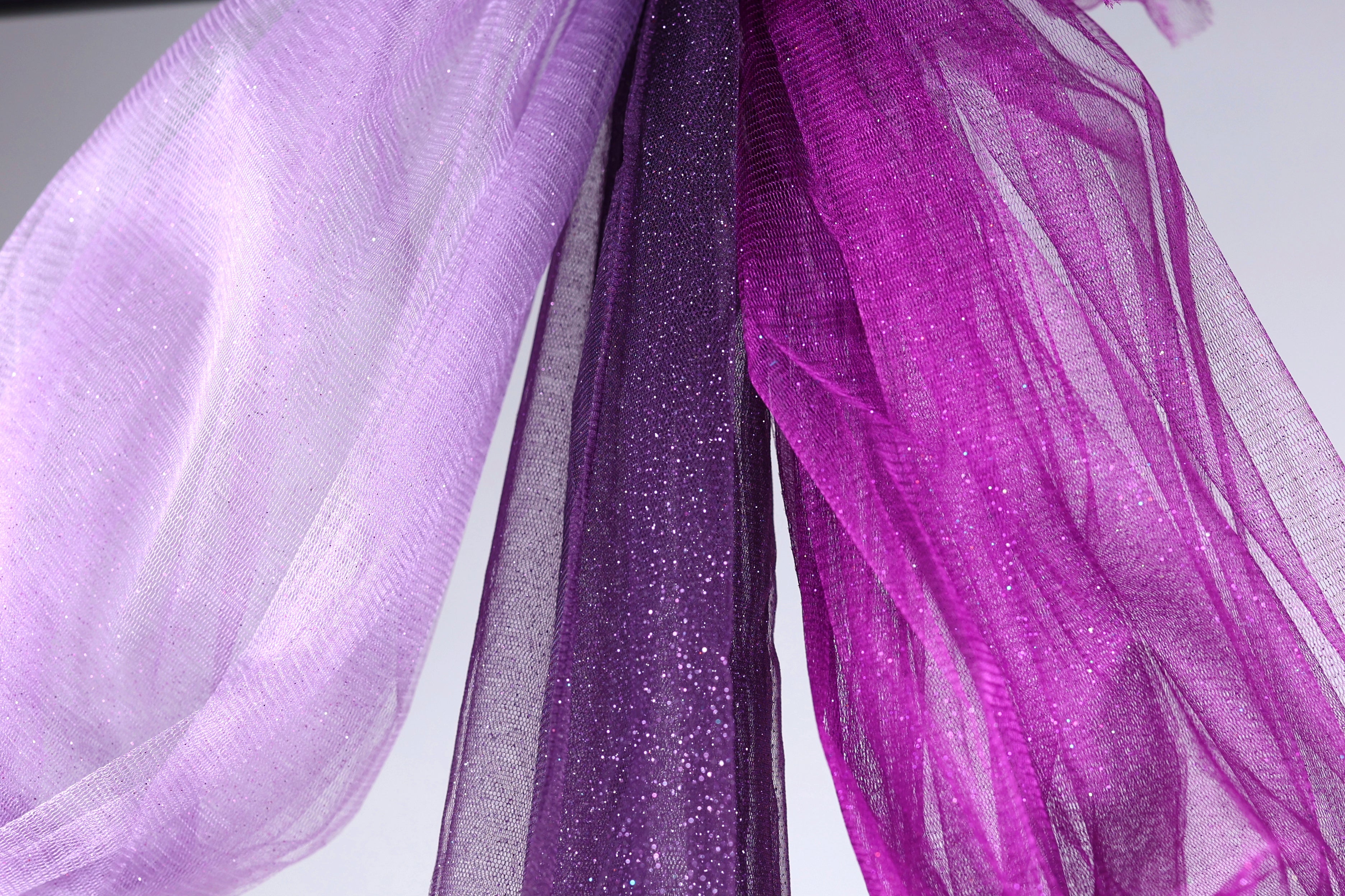 a close-up view of a fabric with a purple and white color scheme, featuring a shiny, glittery texture.