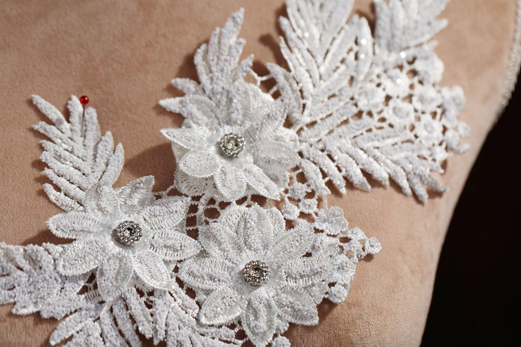 A close-up view of a delicate white lace flower with a small red gemstone in the center, set against a beige background.
