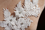 A close-up view of a delicate white lace flower with a small red gemstone in the center, set against a beige background.