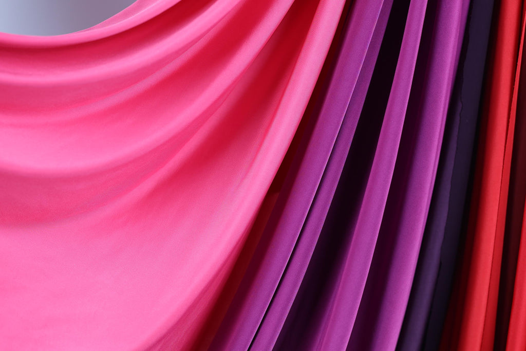 a close-up view of a fabric with a vibrant mix of pink, purple, and red colors. The fabric appears to be a sheer material, with a smooth and flowing texture. The colors are vivid and eye-catching, creating a visually appealing and dynamic composition.