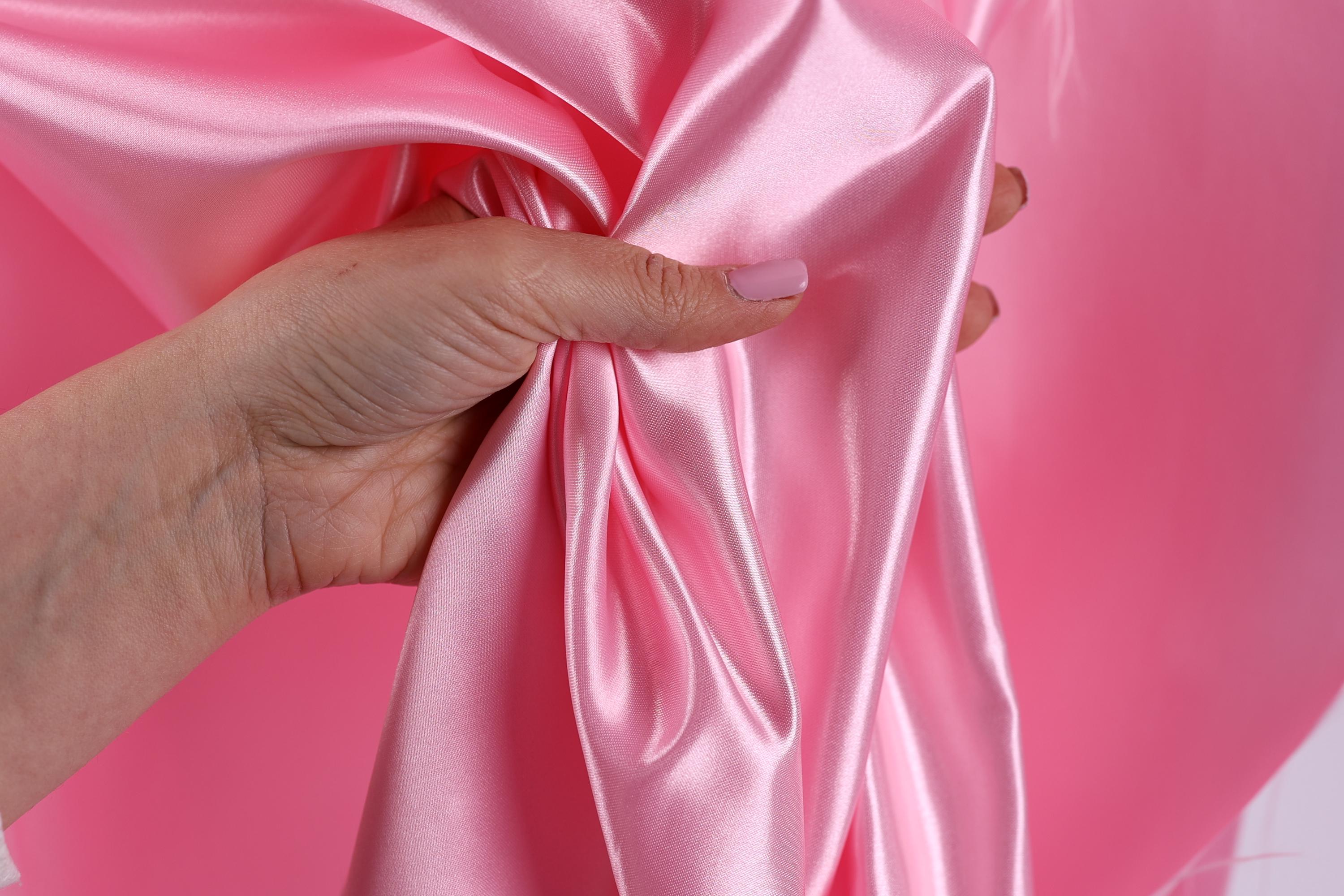 A hand is holding a pink satin fabric, with the fabric partially draped over the hand.