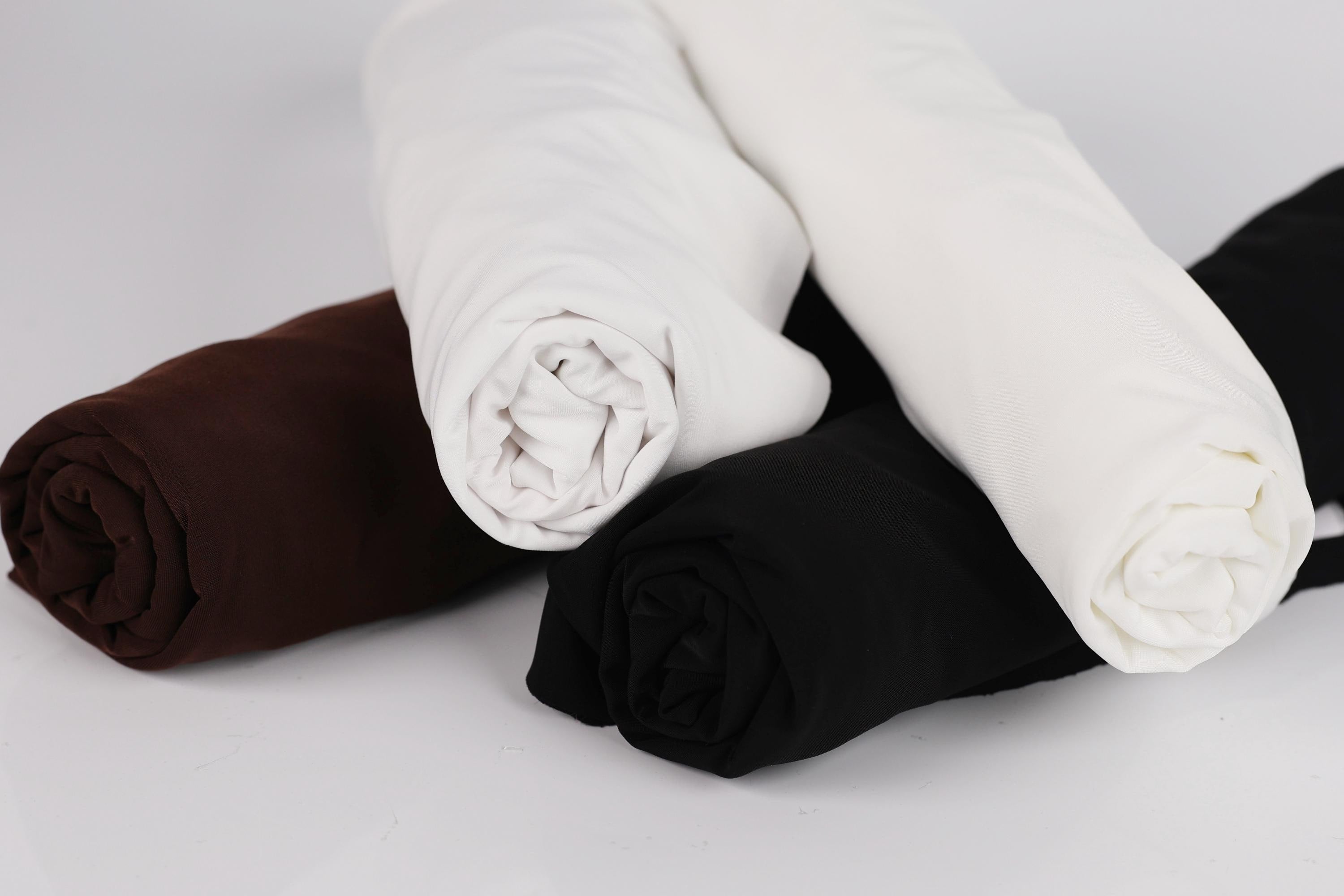 three rolled-up fabric pieces in different colors: brown, white, and black.