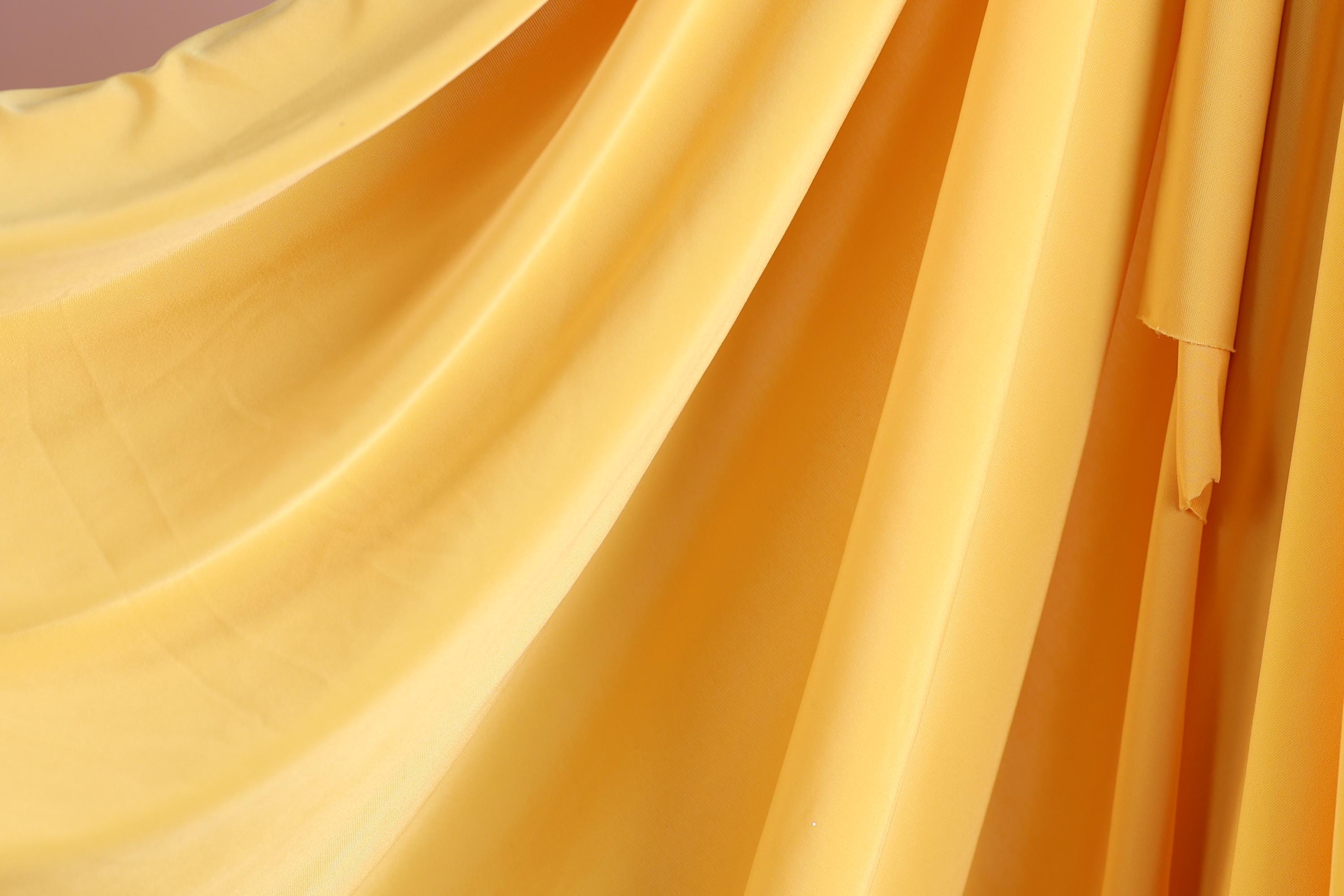 a close-up view of a yellow fabric, possibly a curtain or drape, with a soft, flowing texture.