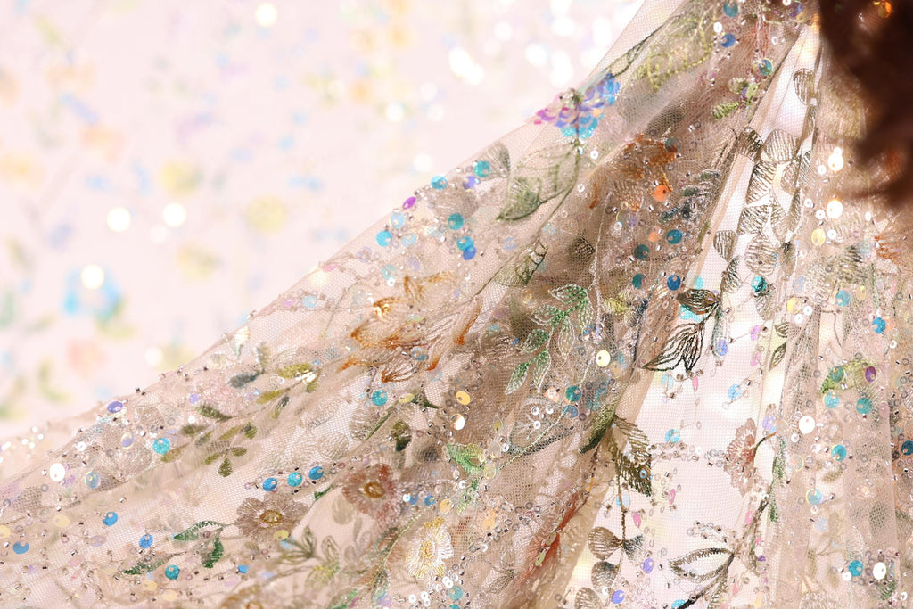 a close-up view of a delicate, intricately embroidered fabric with a floral pattern. The fabric appears to be made of sheer material, giving it a soft and delicate appearance. The embroidery features a variety of colors and patterns, including flowers, leaves, and sequins, creating a visually appealing and detailed design.