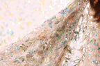 a close-up view of a delicate, intricately embroidered fabric with a floral pattern. The fabric appears to be made of sheer material, giving it a soft and delicate appearance. The embroidery features a variety of colors and patterns, including flowers, leaves, and sequins, creating a visually appealing and detailed design.