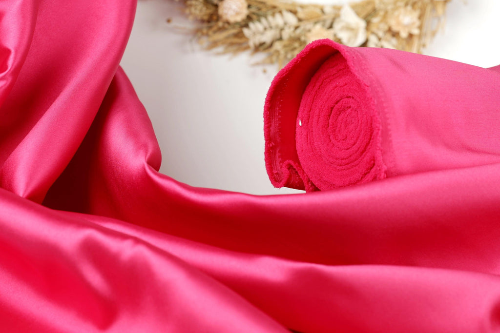 A close-up view of a vibrant pink satin fabric, with a rolled-up piece of the fabric visible in the foreground.