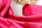 A close-up view of a vibrant pink satin fabric, with a rolled-up piece of the fabric visible in the foreground.