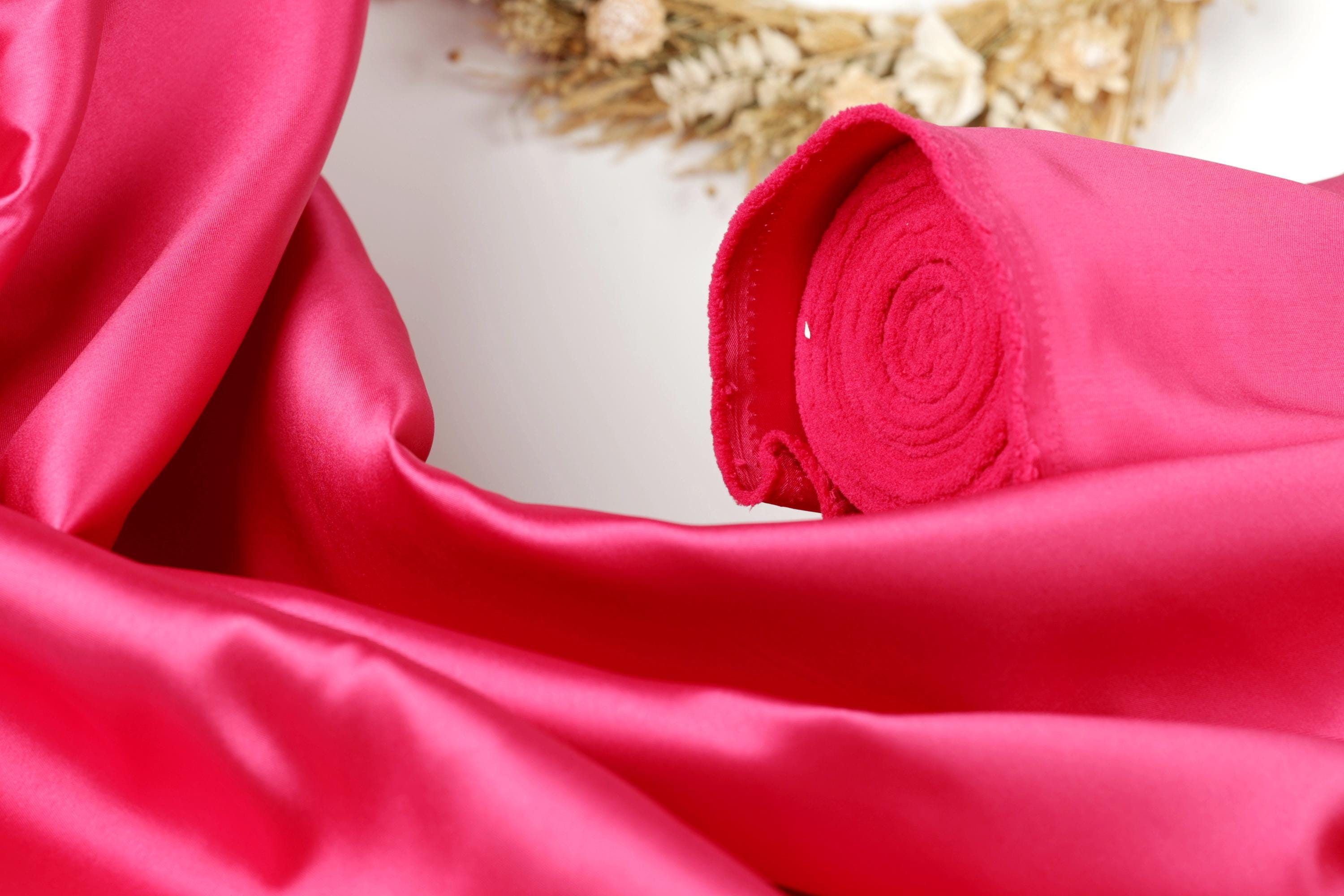 A close-up view of a vibrant pink satin fabric, with a rolled-up piece of the fabric visible in the foreground.