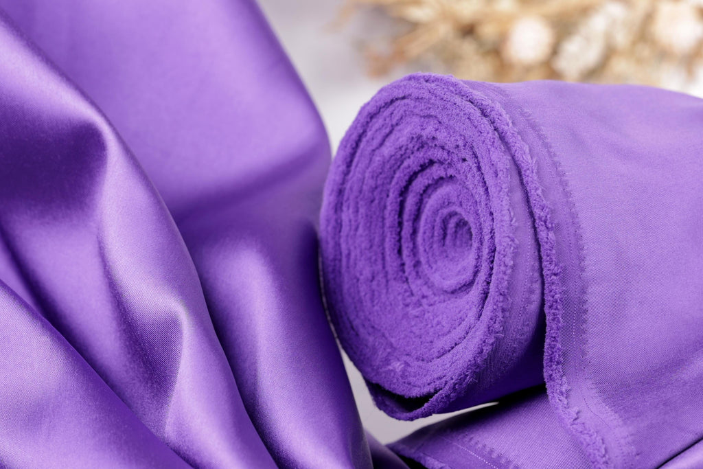 A close-up view of a vibrant purple fabric, possibly silk or satin, with a rolled-up end visible.