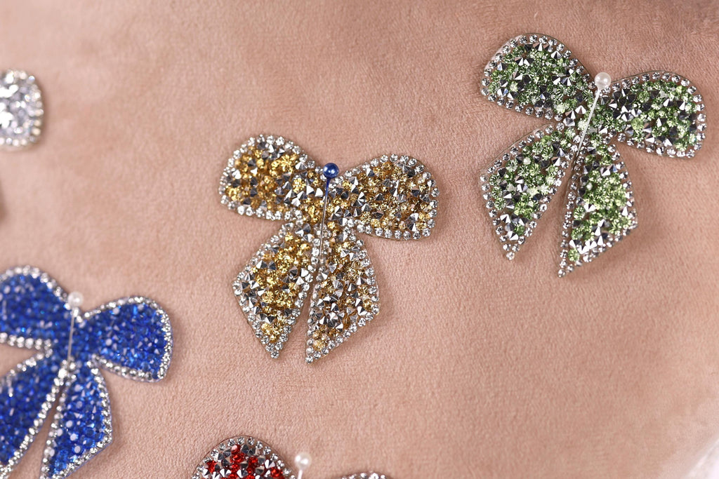 a close-up view of several ornate, sparkling, and colorful jewelry pieces, including a large, eye-catching bow-shaped piece in the center.