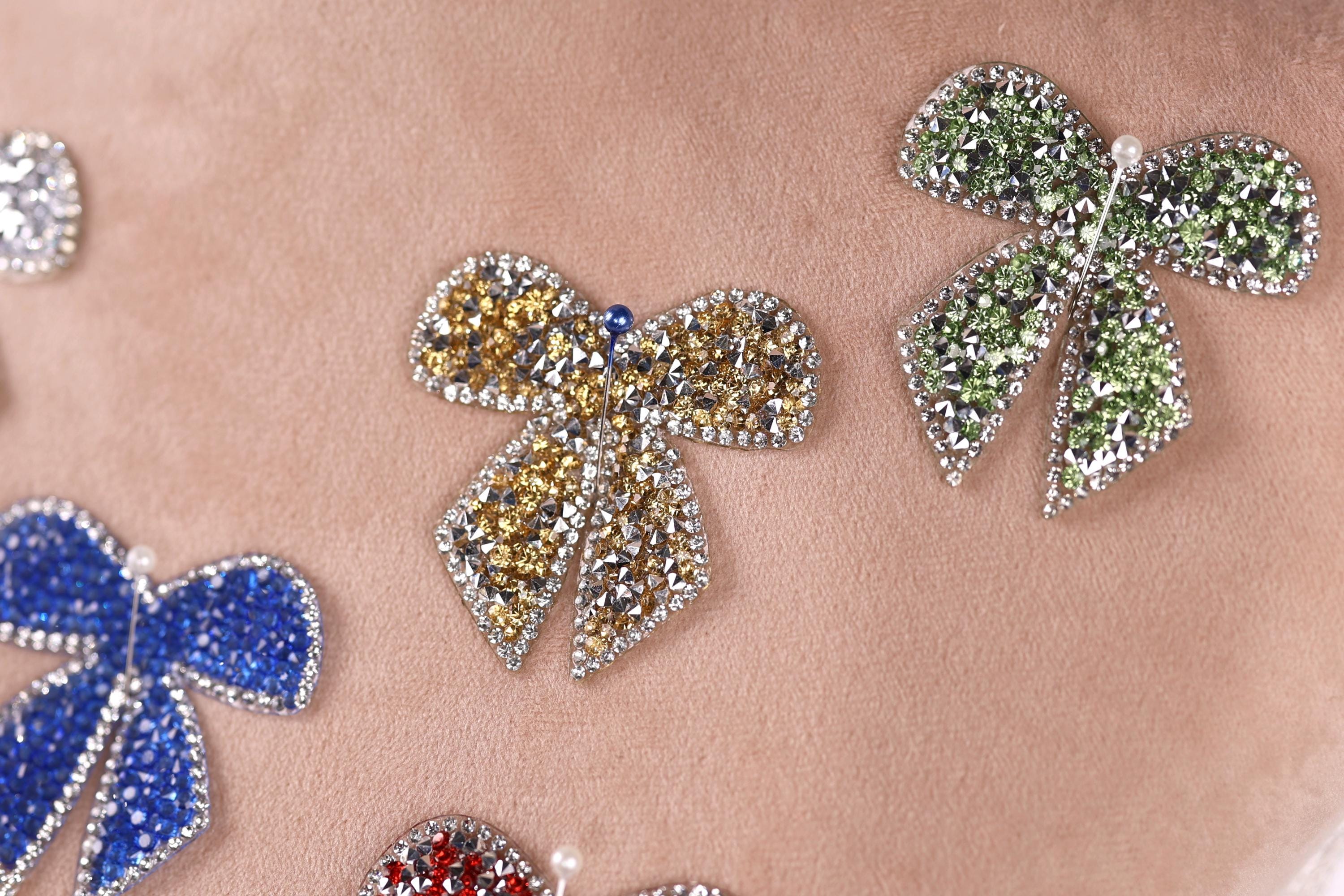 a close-up view of several ornate, sparkling, and colorful jewelry pieces, including a large, eye-catching bow-shaped piece in the center.