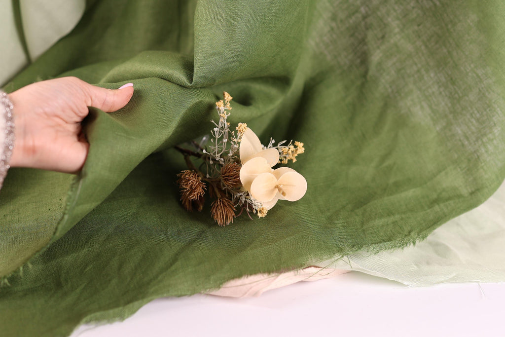 A hand is holding a green fabric, with a small bouquet of white and brown flowers resting on it.