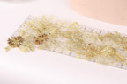 a close-up view of a delicate piece of fabric adorned with gold sequins and flowers, resting on a white surface.
