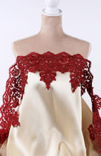 A mannequin wearing a beige dress with red lace trim and a red floral pattern on the bodice.