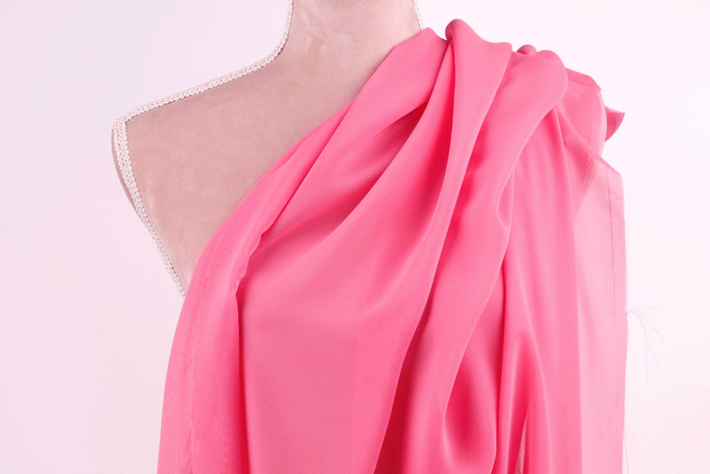 A mannequin wearing a pink one-shoulder dress with a draped, flowing fabric draped over the shoulder.