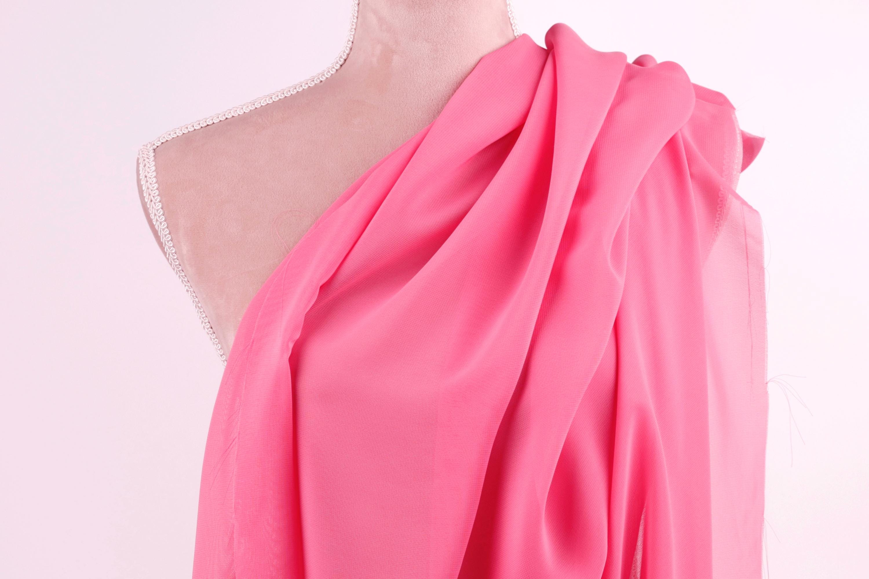 A mannequin wearing a pink one-shoulder dress with a draped, flowing fabric draped over the shoulder.