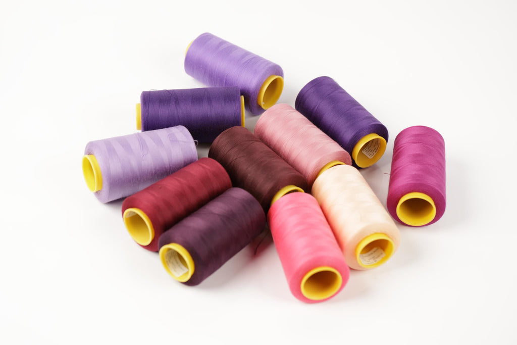 a collection of colorful spools of thread in various shades of purple, pink, and maroon, arranged on a white background.