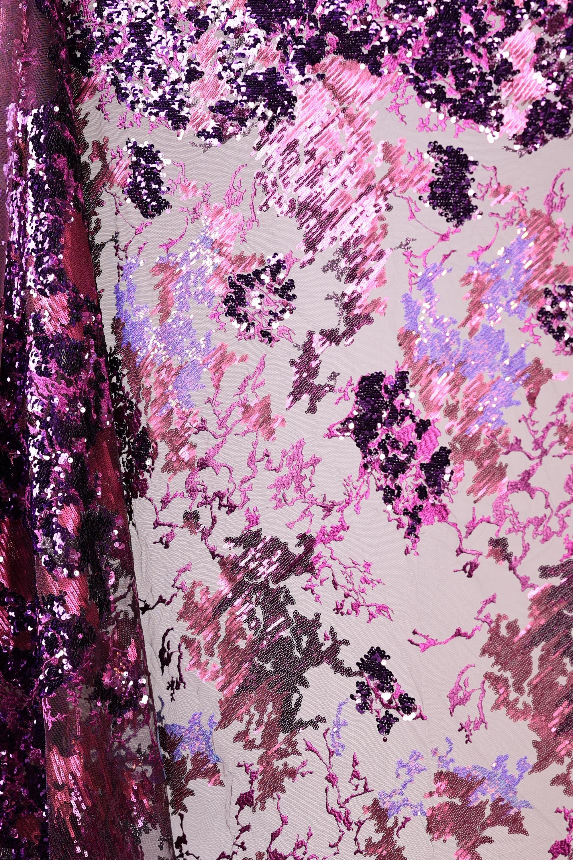 a close-up view of a fabric with a vibrant, multicolored pattern. The fabric appears to be a blend of pink, purple, and black sequins, creating a visually striking and eye-catching design. The pattern is intricate and detailed, with the sequins adding a touch of sparkle and texture to the overall appearance.