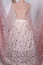 A mannequin wearing a dress with a sheer, pink-colored fabric featuring a leafy, floral pattern.