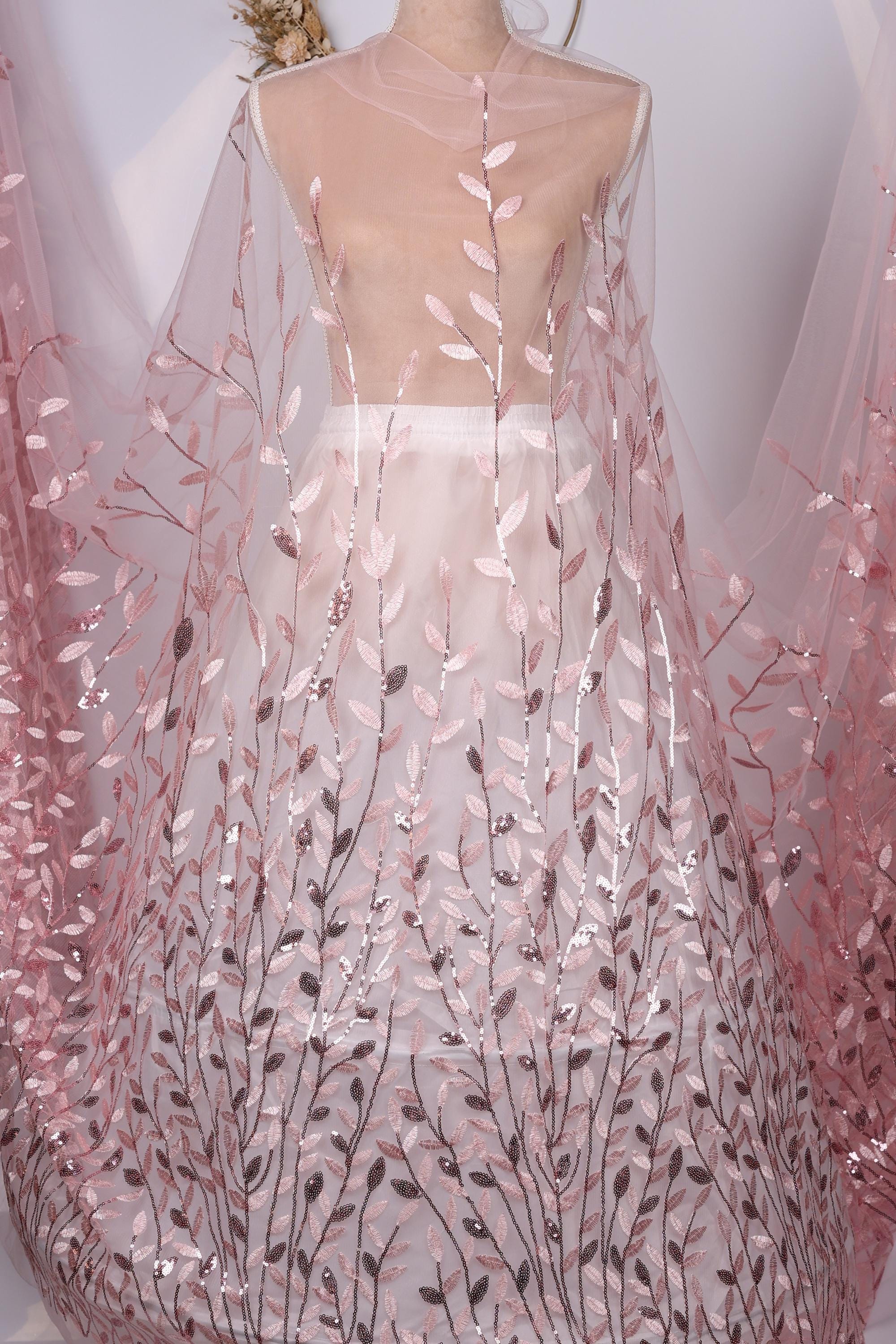 A mannequin wearing a dress with a sheer, pink-colored fabric featuring a leafy, floral pattern.