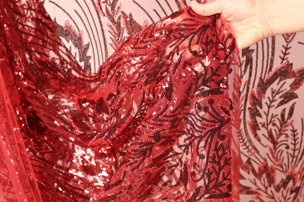 A hand is holding a piece of red sequin fabric with a floral pattern.