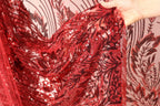 A hand is holding a piece of red sequin fabric with a floral pattern.