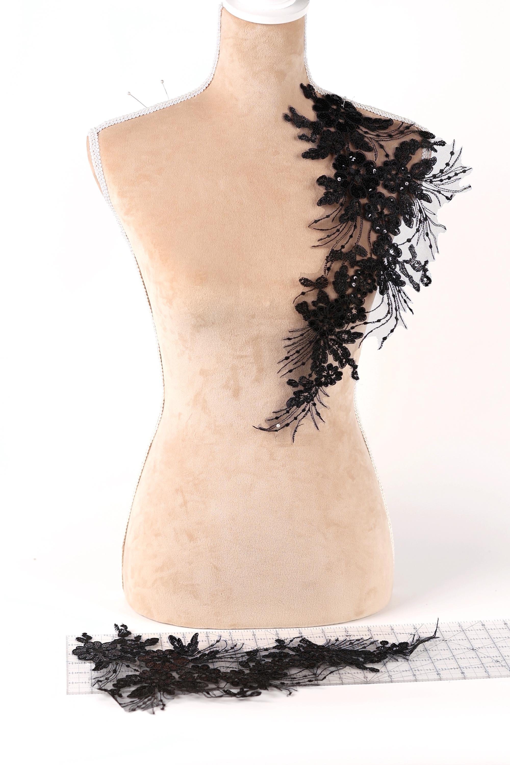 a mannequin with a decorative black lace or sequin embellishment on its shoulder, placed on a white background.