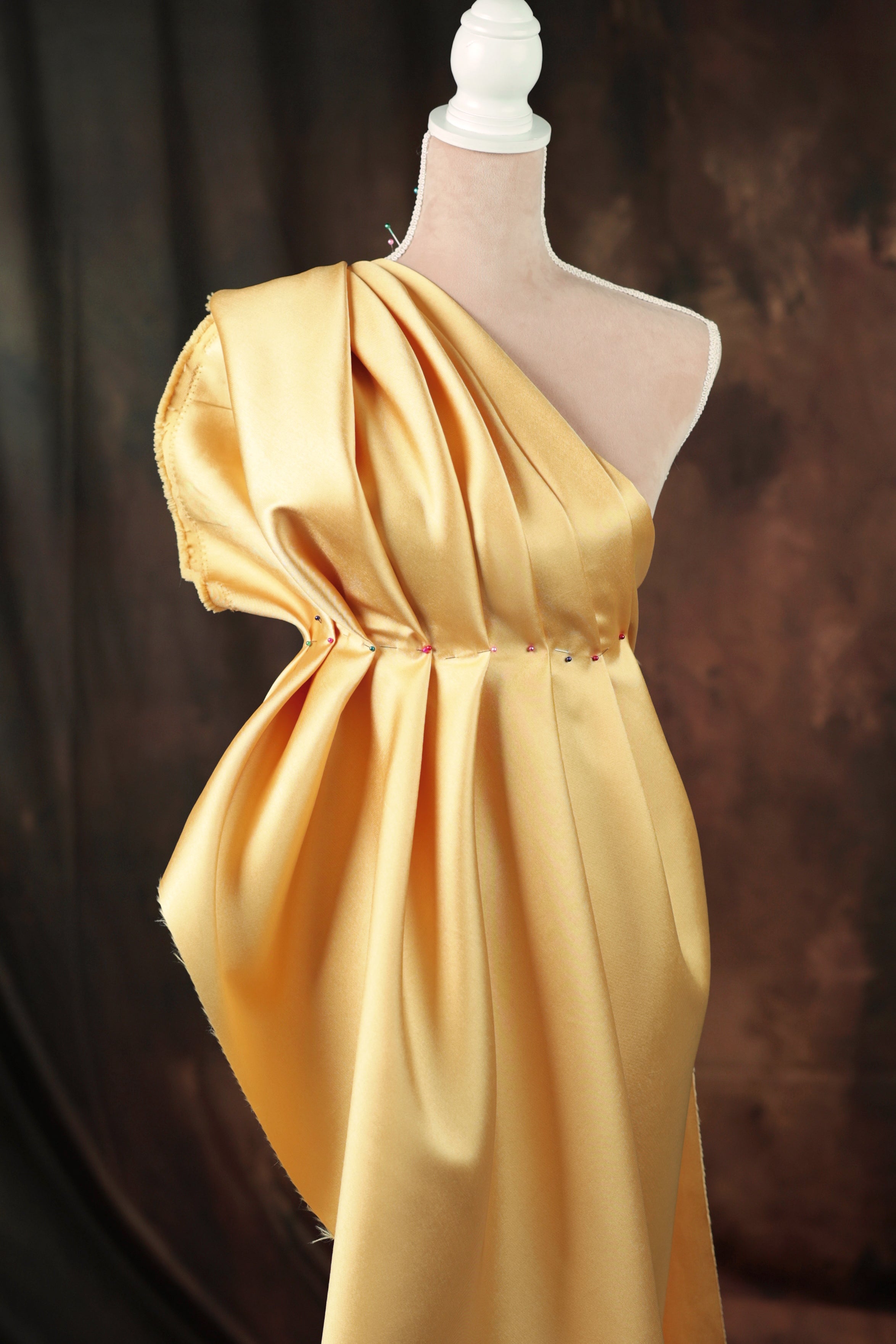 A mannequin wearing a yellow one-shoulder dress with a draped, flowing silhouette.