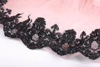 A close-up view of a delicate lace trim with black sequins, creating a visually striking contrast against the pink background.