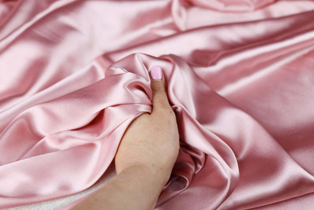 a woman&#39;s hand on a pink satin fabric